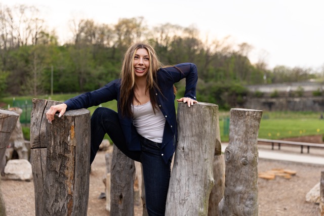 high school senior girl posing on a natural wood playscape