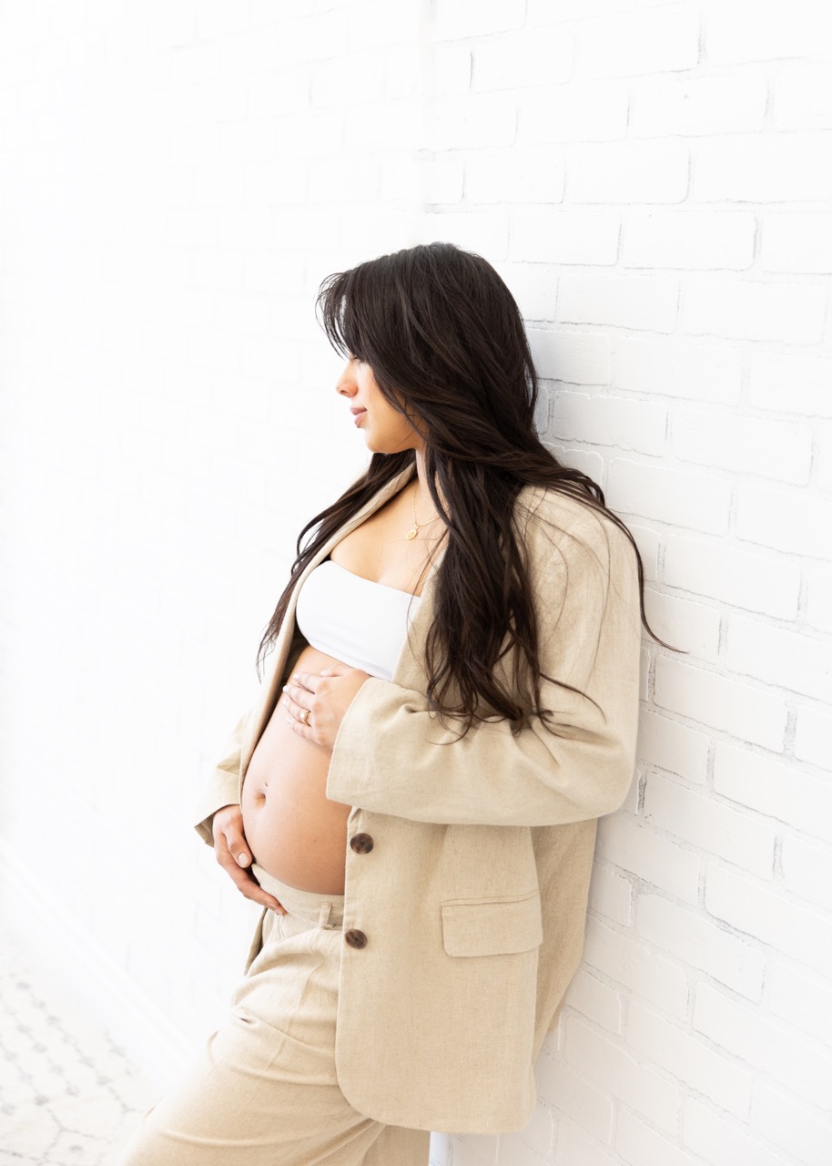 beautiful brown hair expecting mom to be in a tan suit and shite top holding her belly