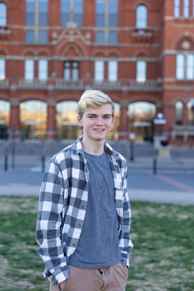 Young man smiling in front of a red brick building.