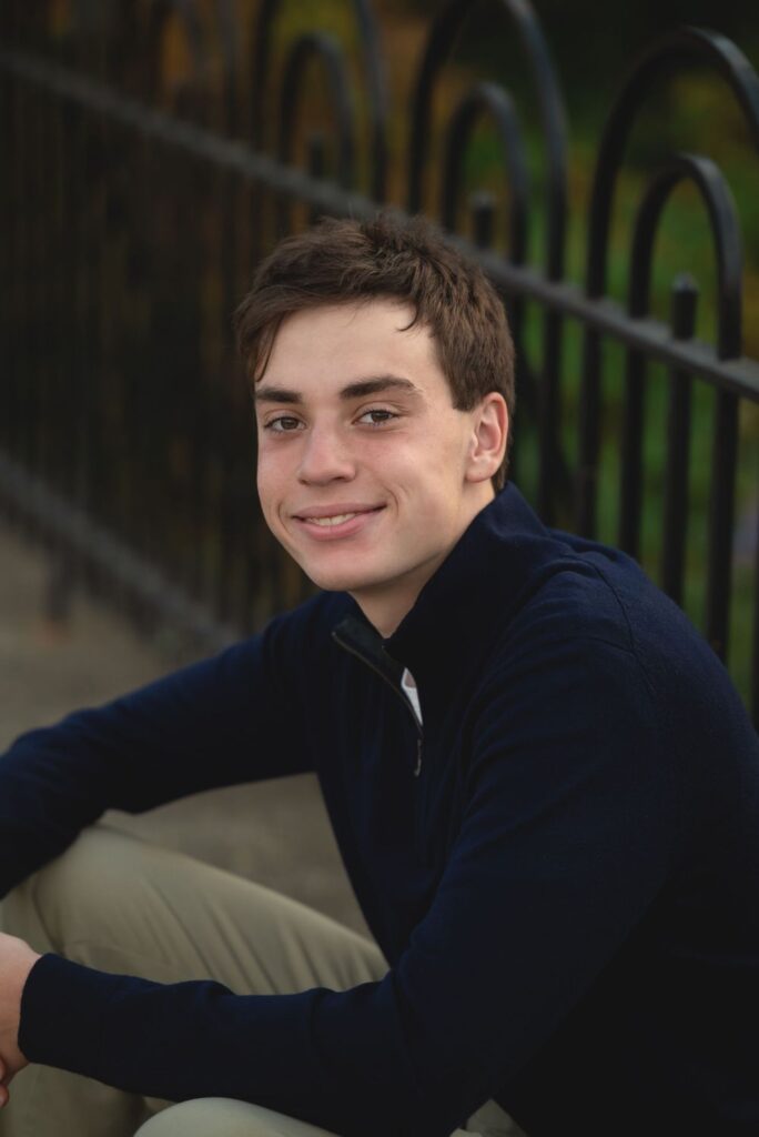 A young man sitting on a railing with a smile on his face.