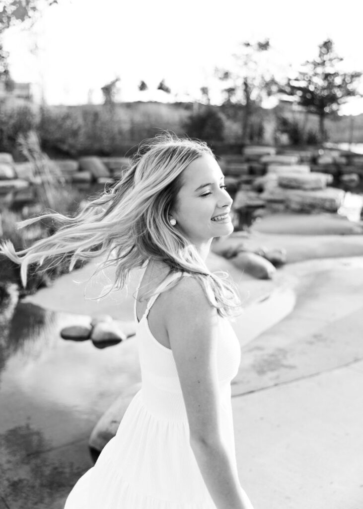 A black and white image of a smiling young woman with her hair blowing in the wind outdoors.