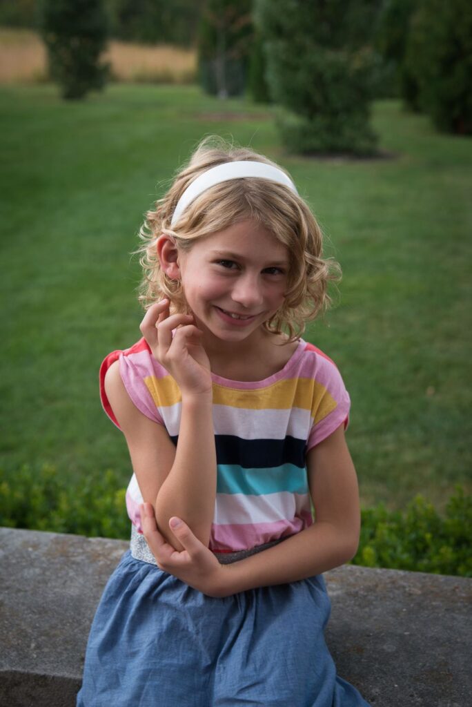 Young girl with a headband smiling and sitting outdoors.