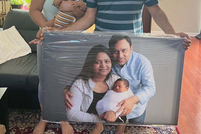 A family holds a large framed portrait of themselves with a newborn baby.