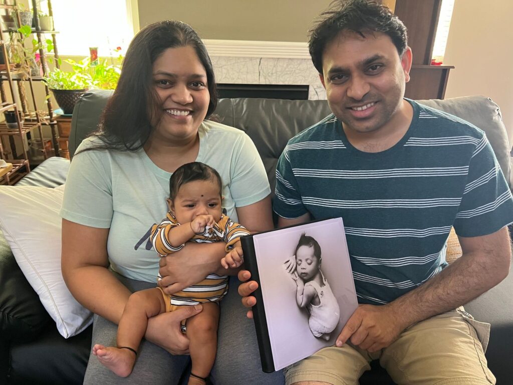 A family sitting together with a baby in arms and holding a photo book featuring an image of the baby.