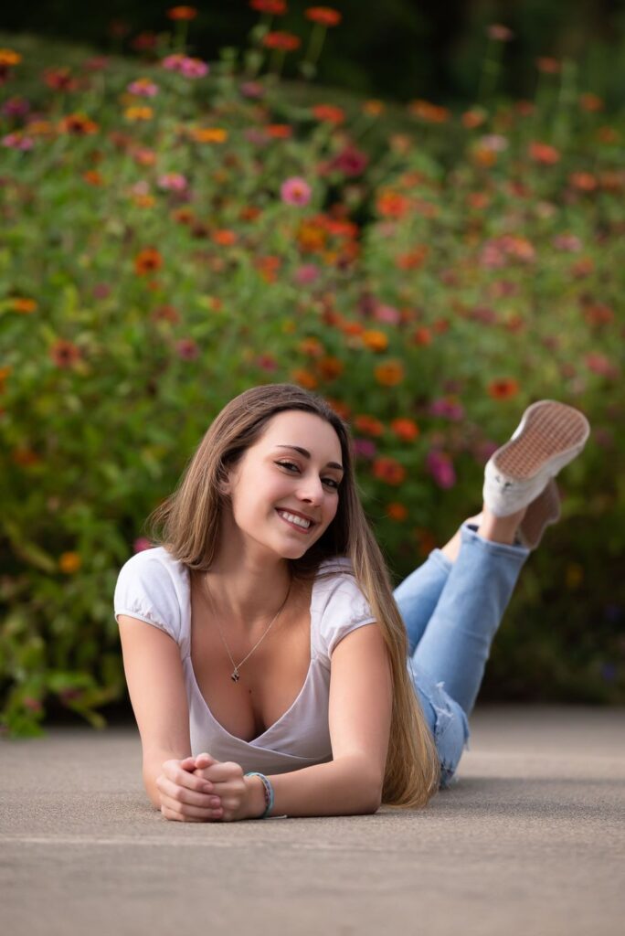 Young woman lying on her stomach and smiling in front of a garden with colorful flowers.