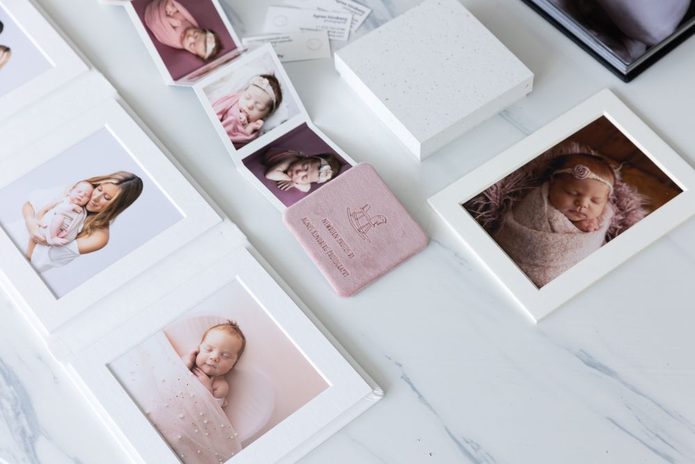 A collection of professional newborn and family photographs displayed on a marble surface.