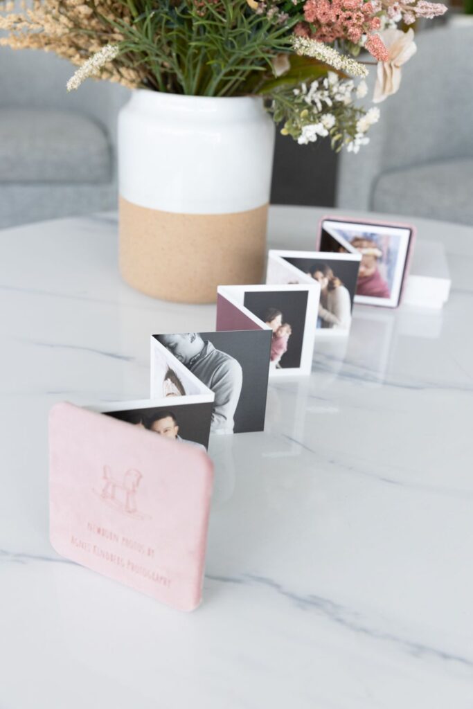 Miniature photo albums with family pictures displayed on a marble countertop beside a vase with flowers.