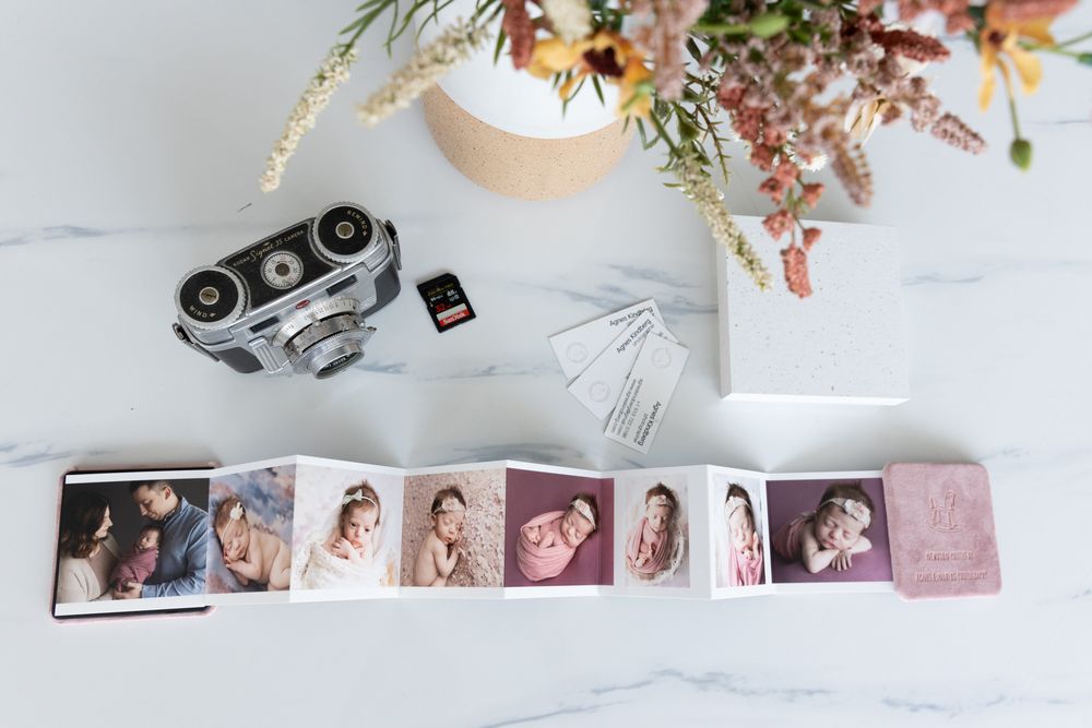 Flat lay of a vintage camera, memory card, and an accordion photo book with family portraits on a marble surface, accompanied by a vase with flowers.