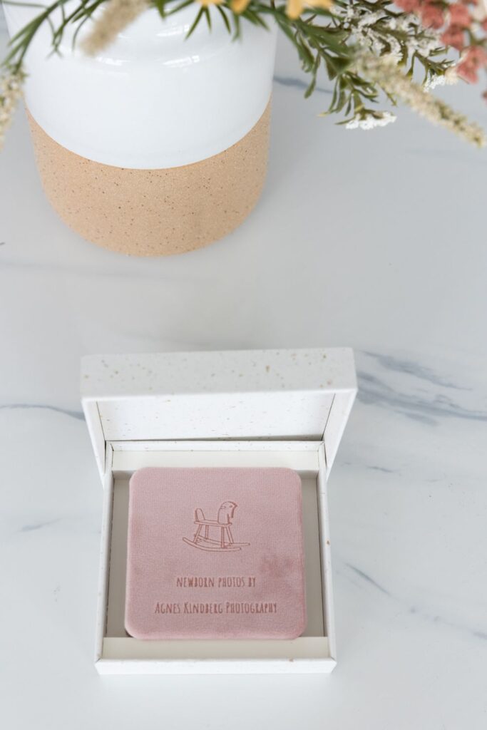 A personalized pink wedding photo album in a white presentation box on a marble surface, with a floral arrangement and a two-tone vase in the background.