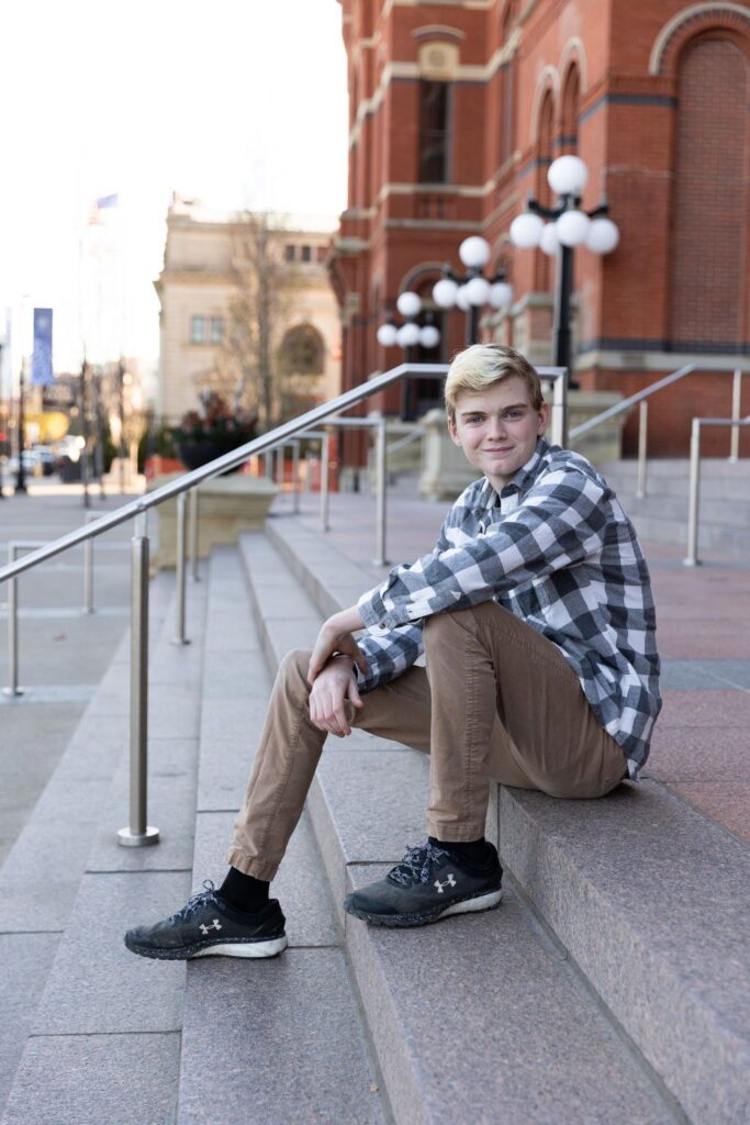 Young man sitting on outdoor steps, smiling at the camera.