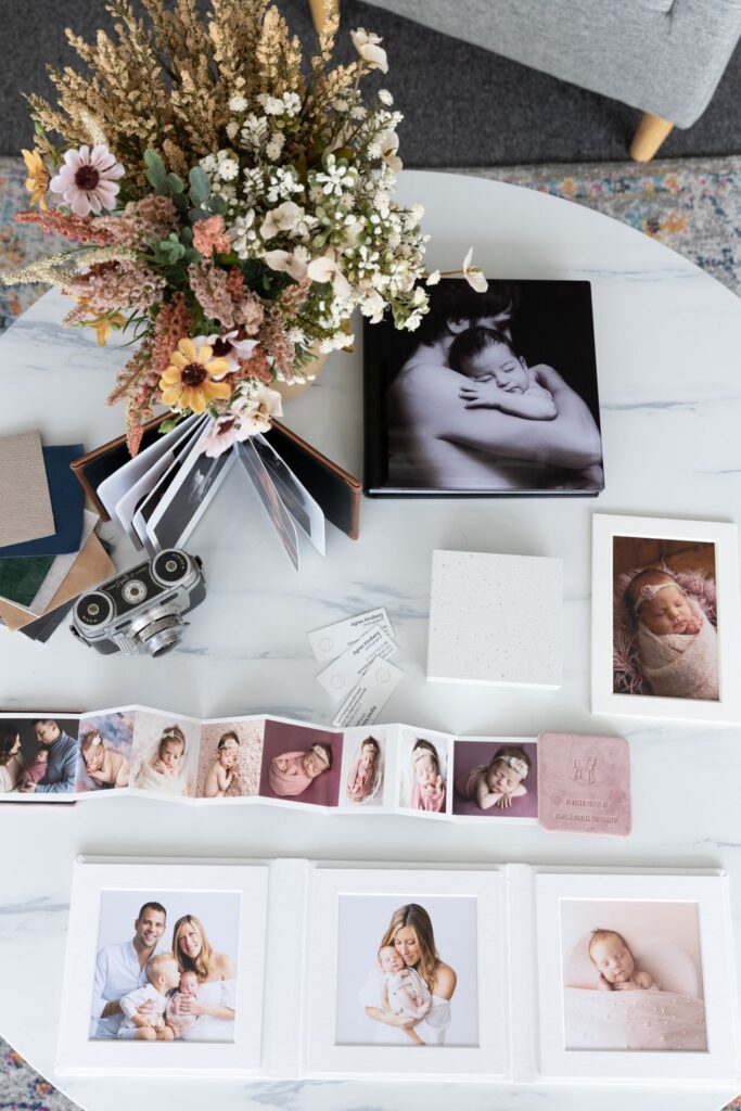 Photography portfolio displayed on a table featuring family photos, baby portraits, and a vintage camera, with a floral arrangement as the centerpiece.