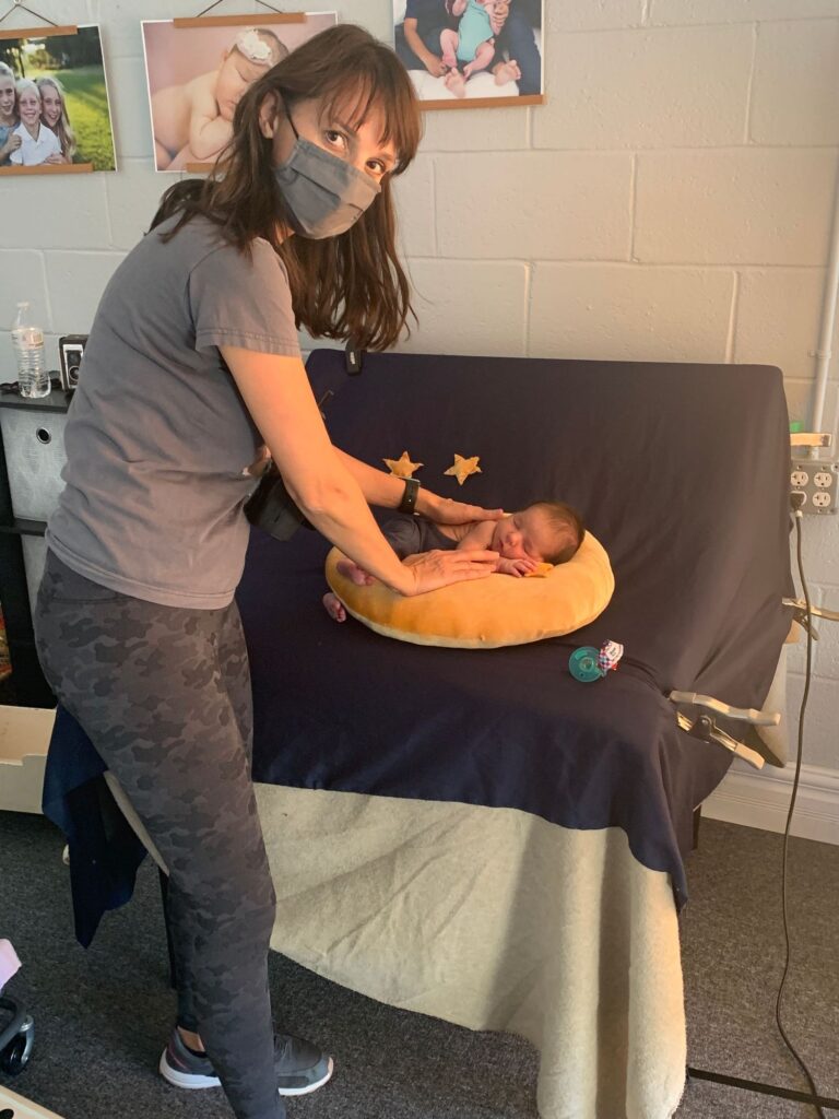 A woman wearing a mask, sensitive to Infertility Awareness, tends to an infant on a changing table.