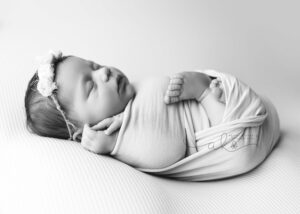 Newborn baby wrapped in cloth, sleeping peacefully with a floral headband.