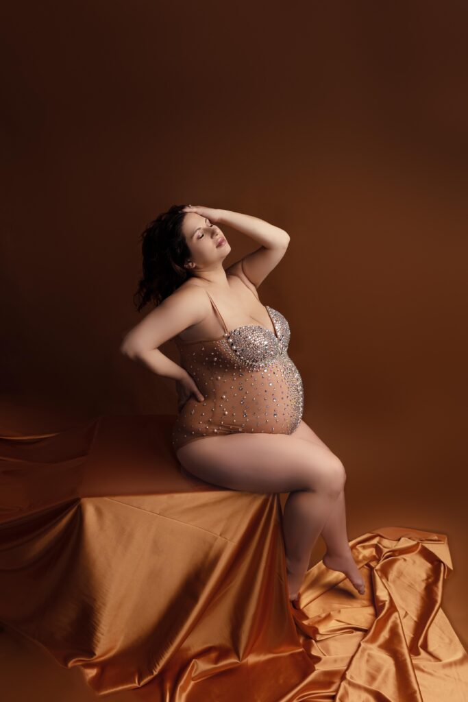 Pregnant woman posing in embellished dress on brown backdrop.