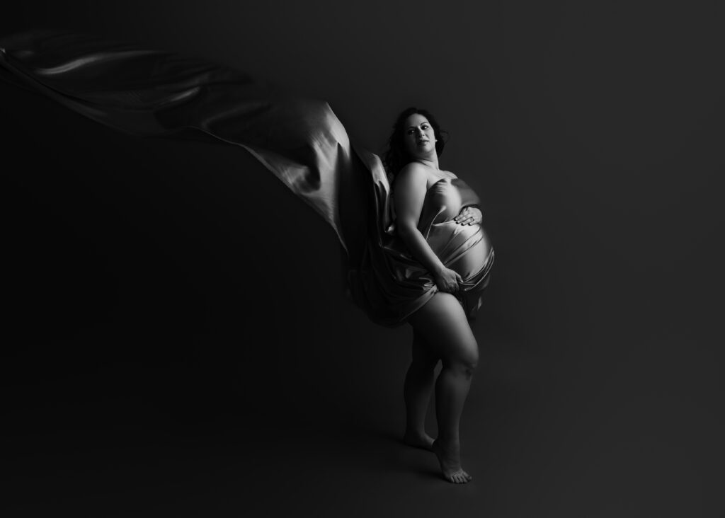 Pregnant woman with flowing fabric, artistic black and white.