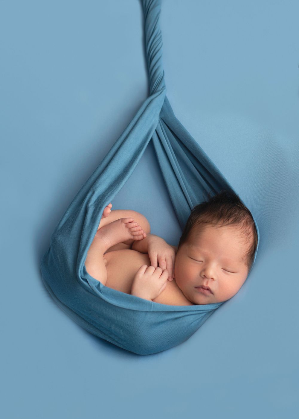 modern newborn photography A newborn baby sleeping peacefully in a blue cloth hammock.