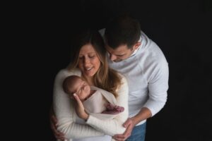 A couple gently holding and looking at their newborn baby with affection.