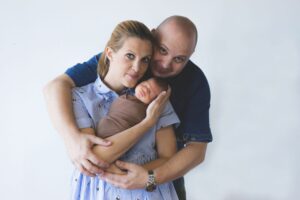 Couple embracing their sleeping newborn baby.