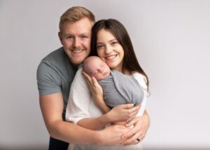 A smiling couple holding a sleeping newborn baby wrapped in a cloth.