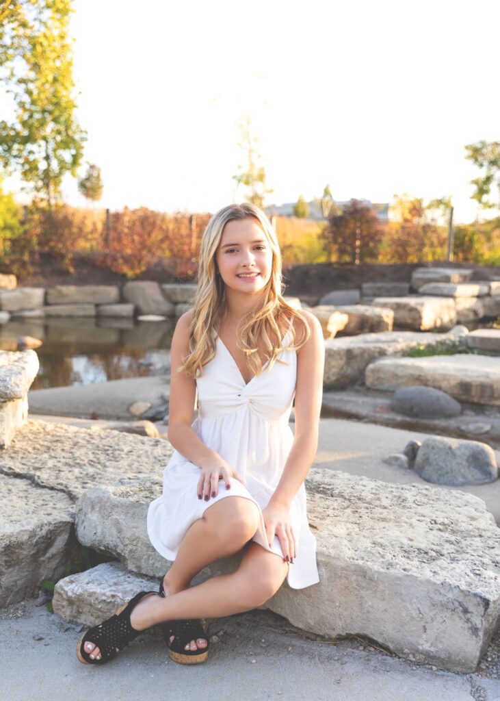 Woman sitting on rock outdoors in white dress.