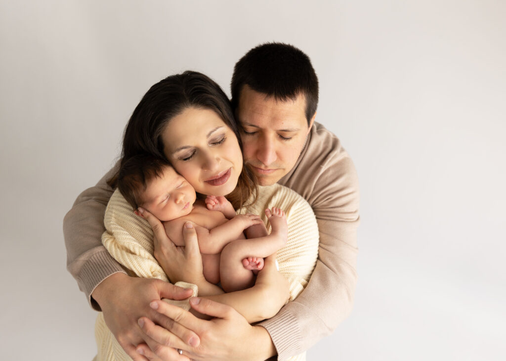 A tender moment of parents cuddling their newborn baby, as they embrace closely with expressions of love and affection.