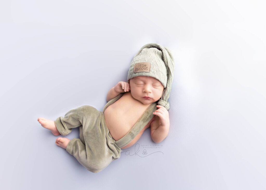 Newborn in green outfit and sprout hat sleeping.