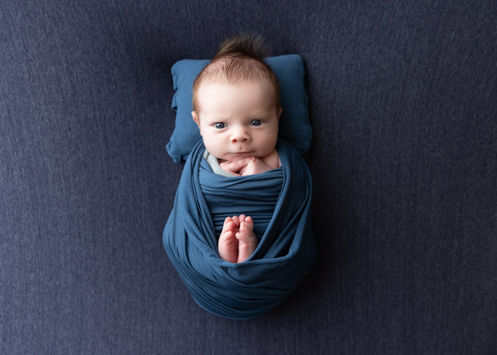 Swaddled newborn with thoughtful gaze on blue blanket.