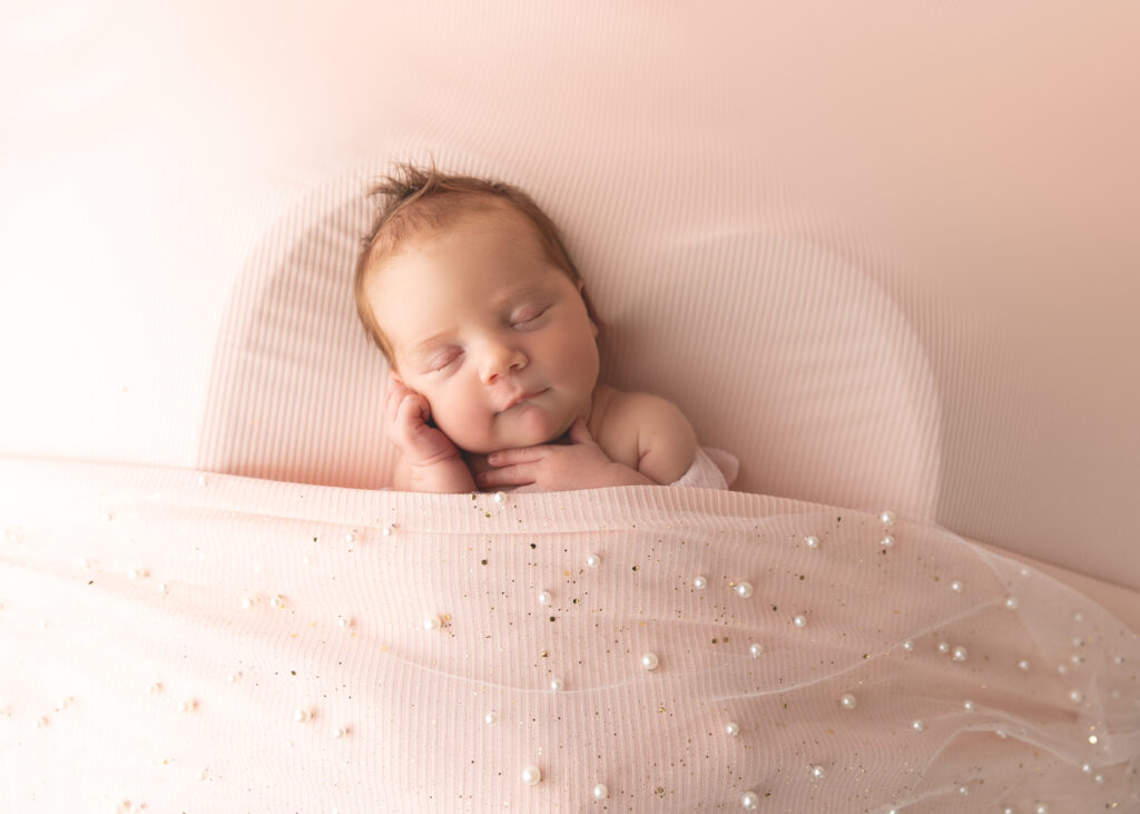 Newborn baby sleeping peacefully on a pink blanket.