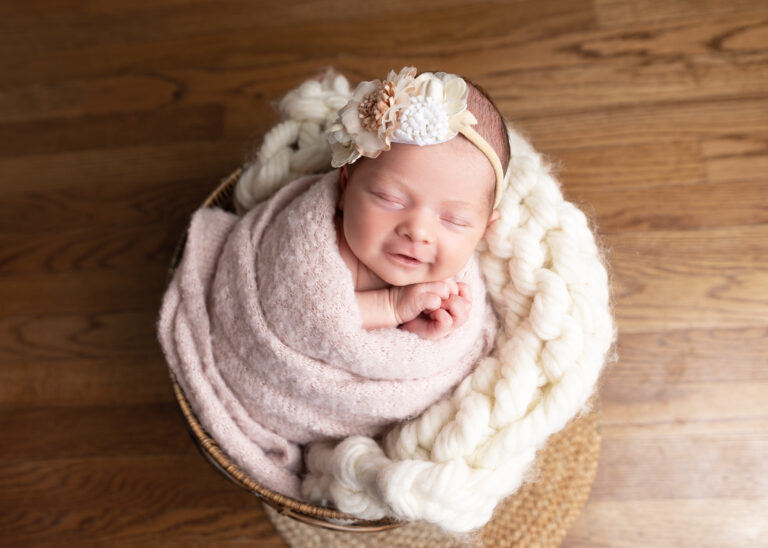 Newborn baby sleeping in basket with floral headband.