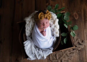 Newborn baby wrapped in white, sleeping in wooden basket.