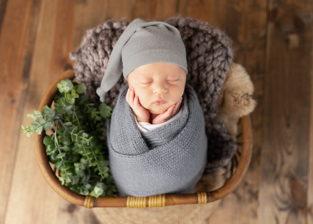 Newborn baby sleeping in basket with knitted blanket.