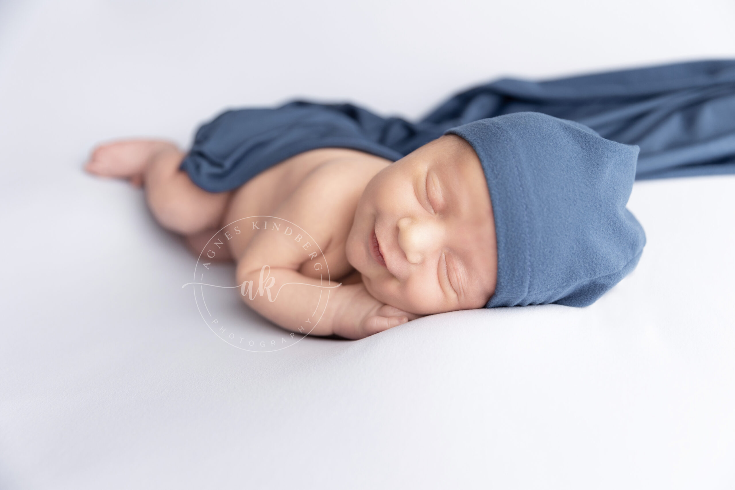 newborn baby side sleeping in blue sleepy hat and matching wrap by Agnes Kindberg Newborn Photographer