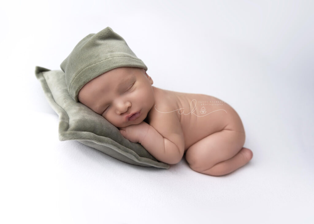 Newborn baby in Taco Pose with green velvet sleepy hat and matching pillow set