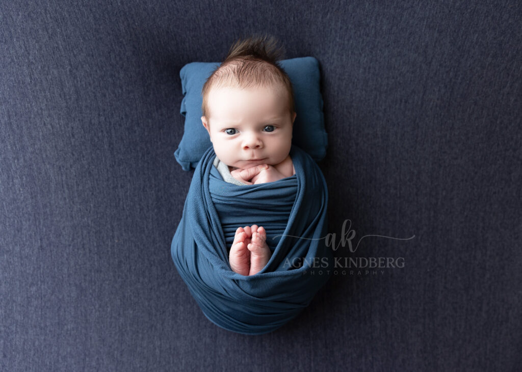 newborn babu wrapped in blue matching set of pillow, eyes open