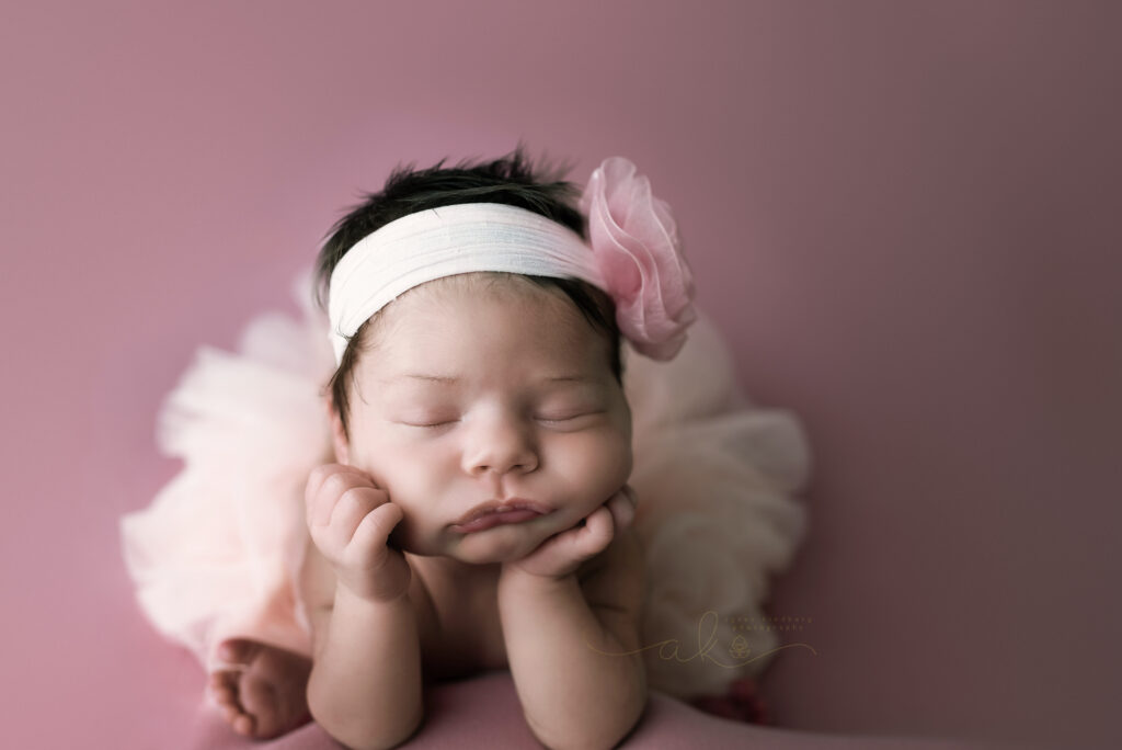 newborn baby girl sleeping hands under chin in Froggy Pose, with pink headband and tutu