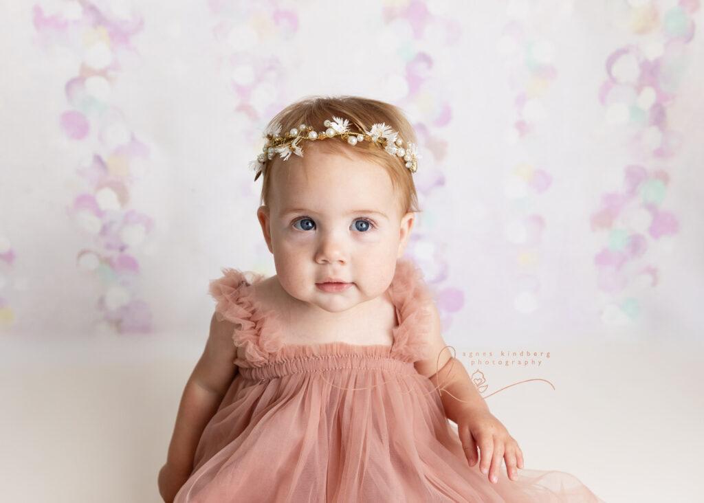 one years old baby girl in pink dress and floral headband