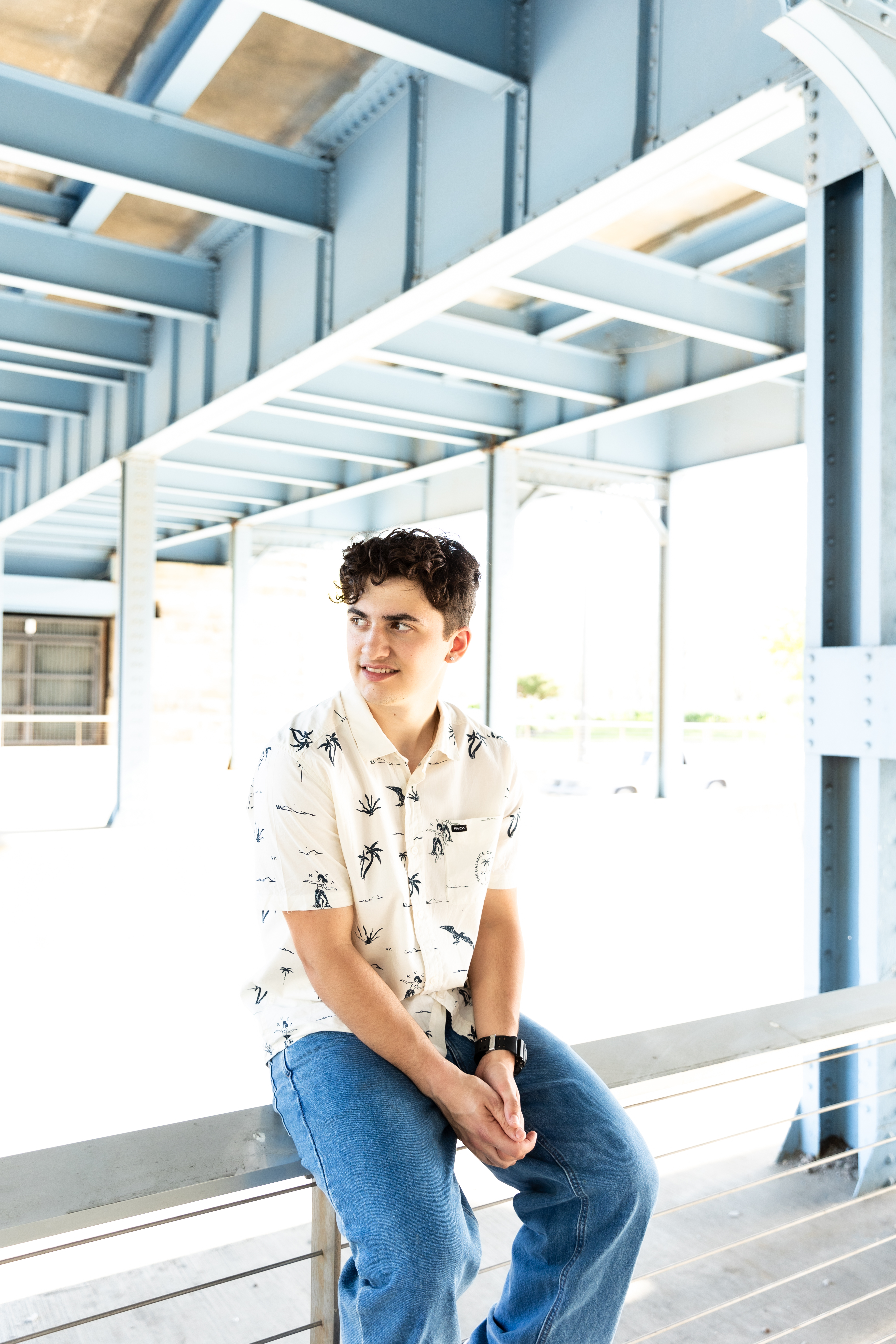 high school senior Mateo sitting on fence under the Roebling Bridge Downtown Cincinnati