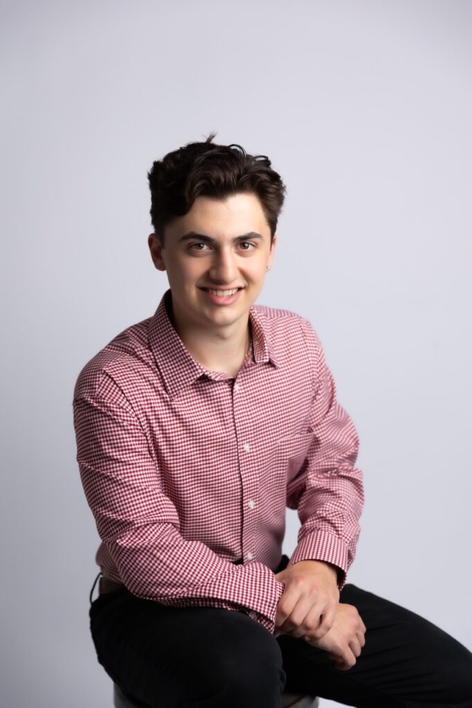 High School senior boy sitting on chair arms crossed in red shirt