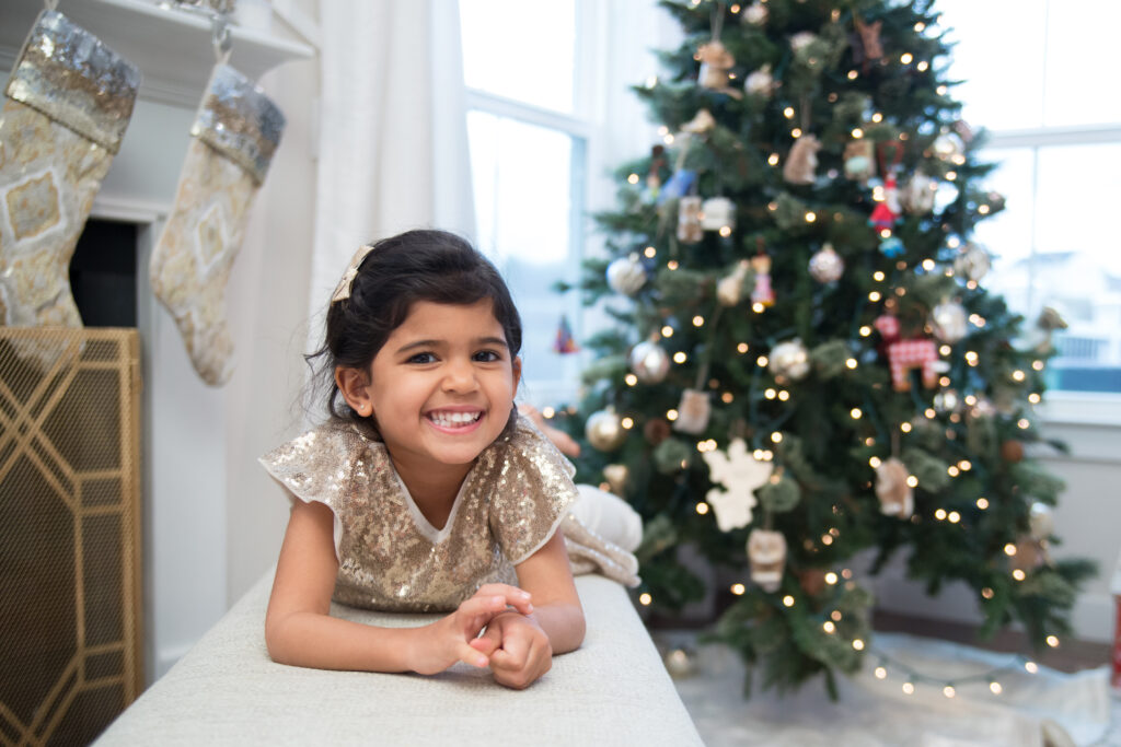 little girl dressed up, laying on bench, smiling in front of Christmas tree