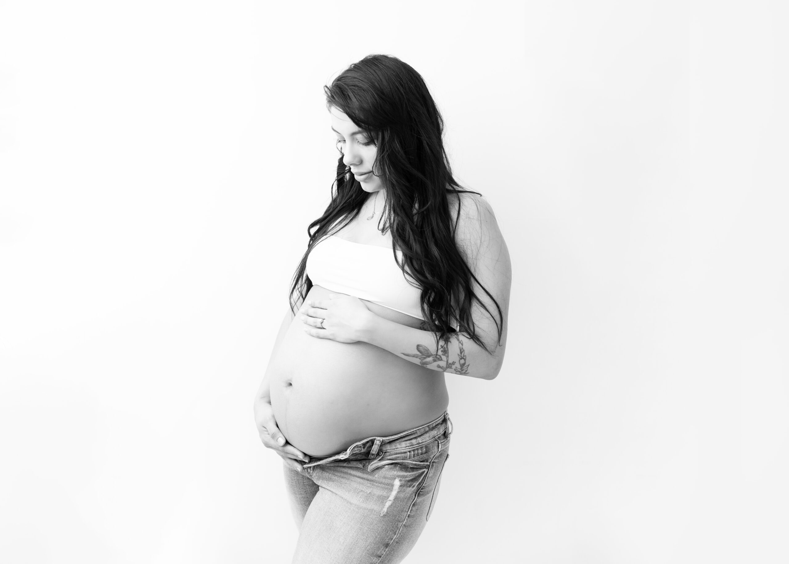 pregnant women posing, holding her belly in a white tank top and unbuttoned jeans