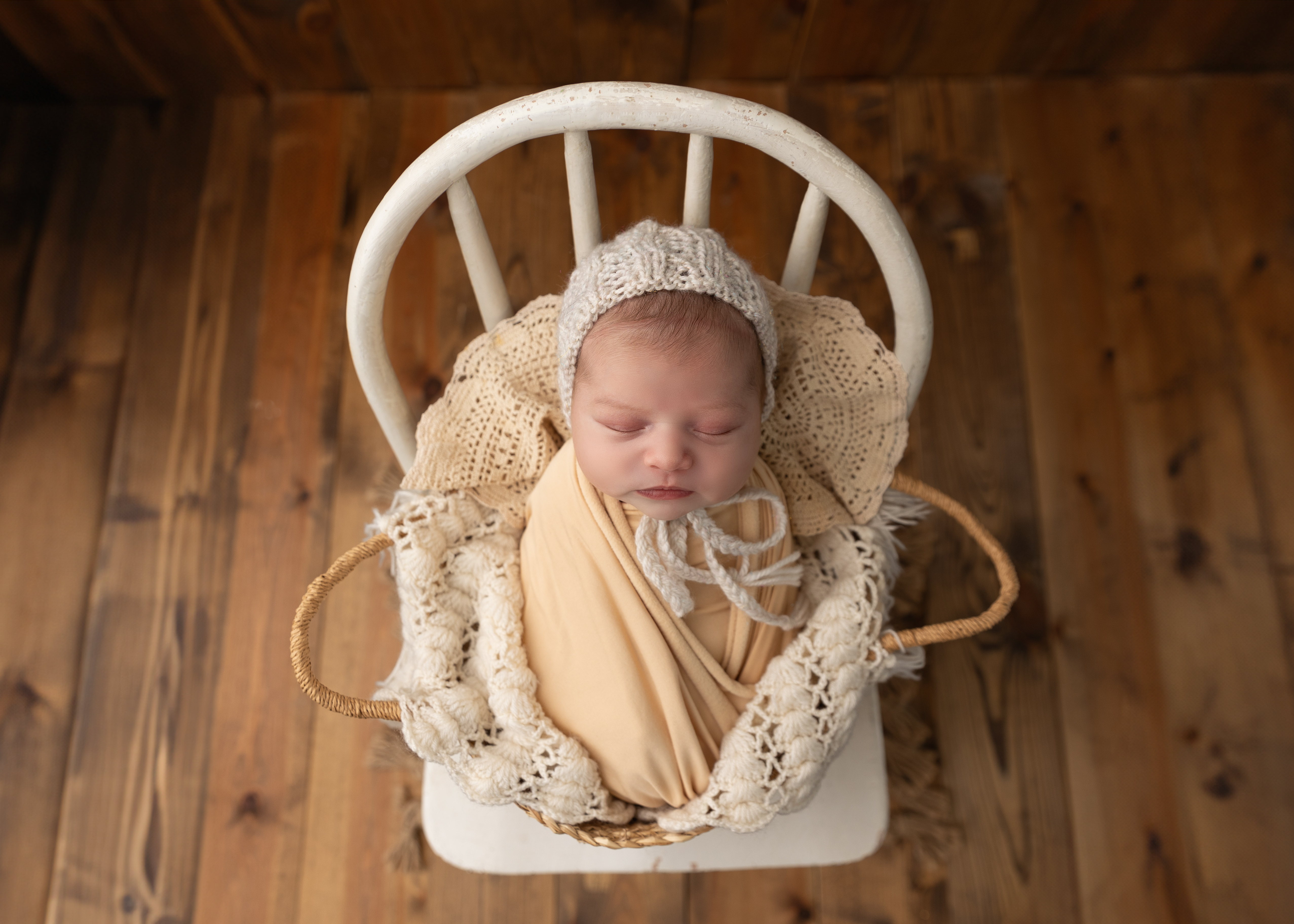 newborn baby girl wrapped in white and cream sleeping in a basket on a chair