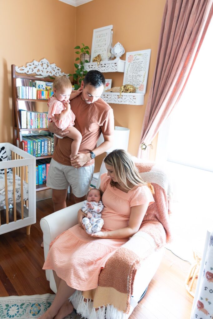 mom sitting in chair holding baby on nursery, dad holding toddler