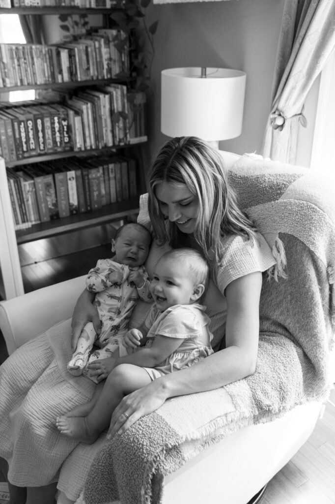 mom snuggles newborn and toddler in chair in a nursery 