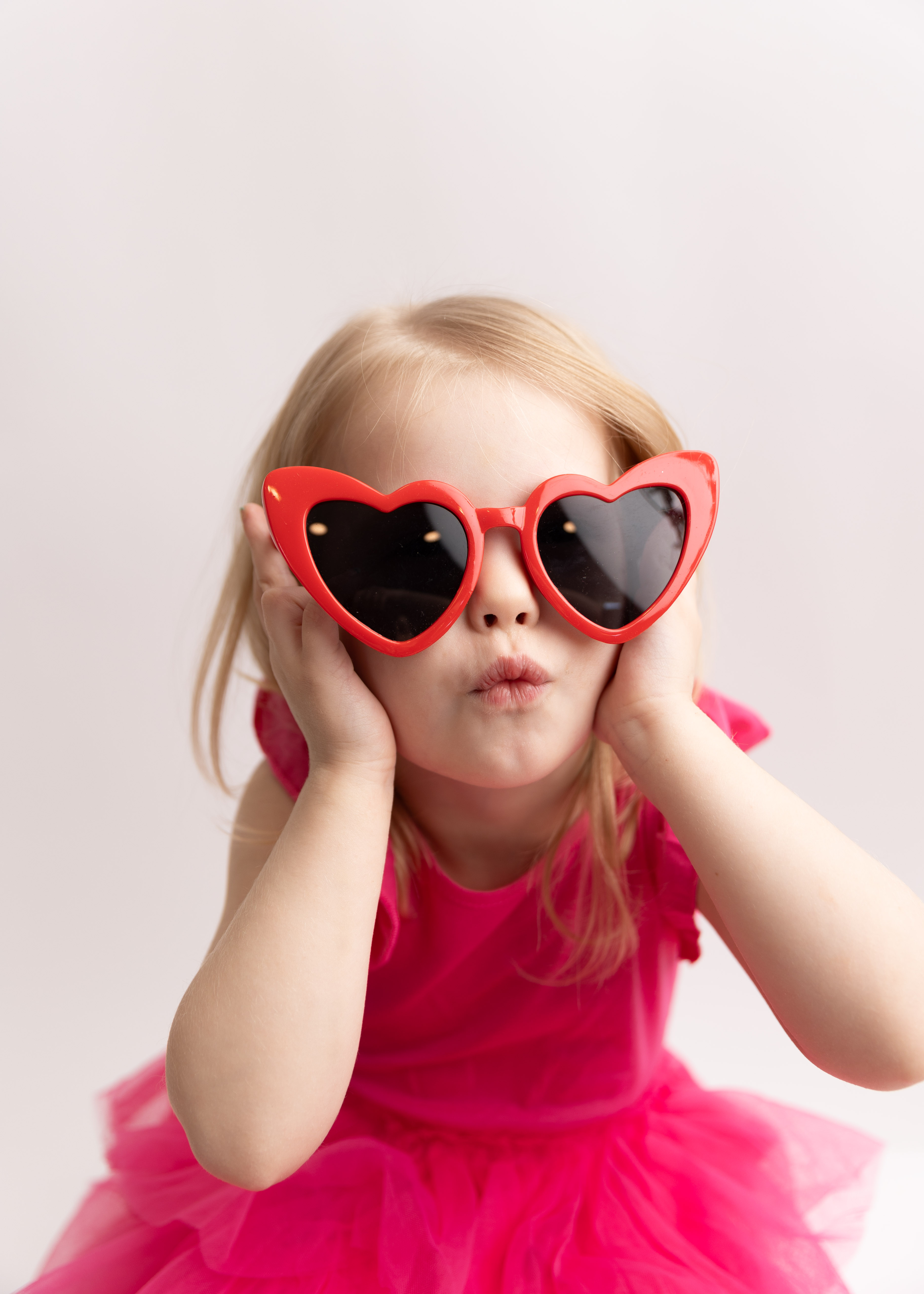 little girl in red heart glasses making cute face