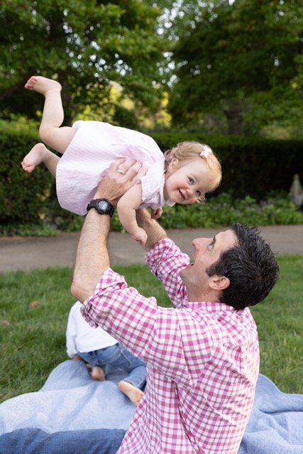 dad playing airplane with baby girl on a blanket at Ault Park